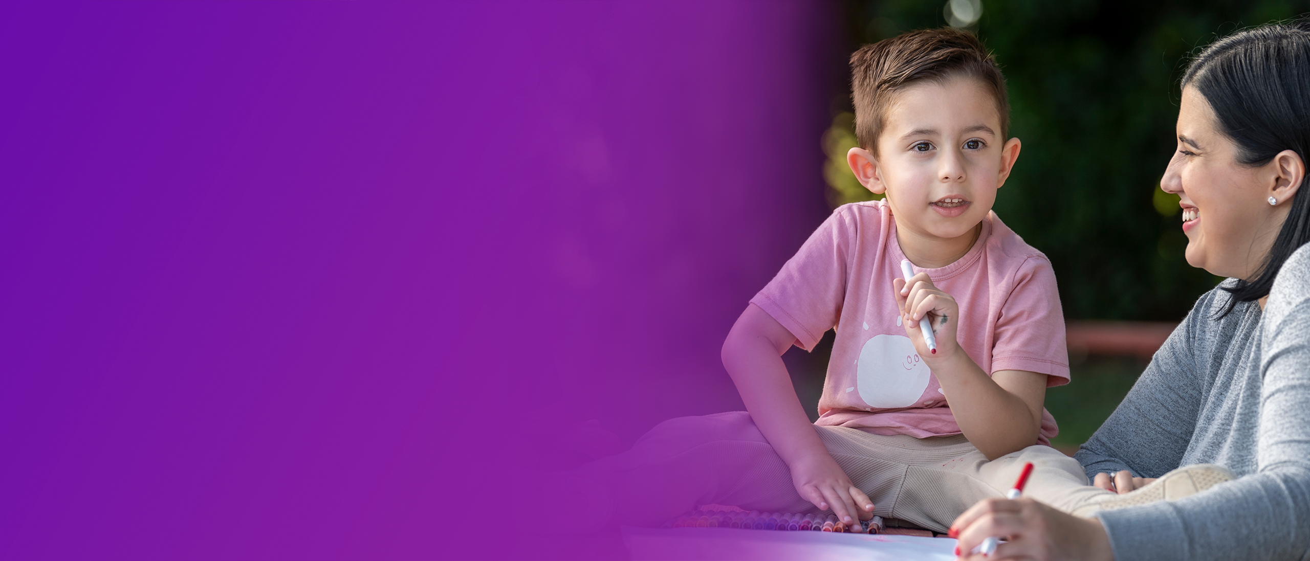 Matteo, a child with SMA, sitting upright on a picnic blanket with his mom holding a red marker