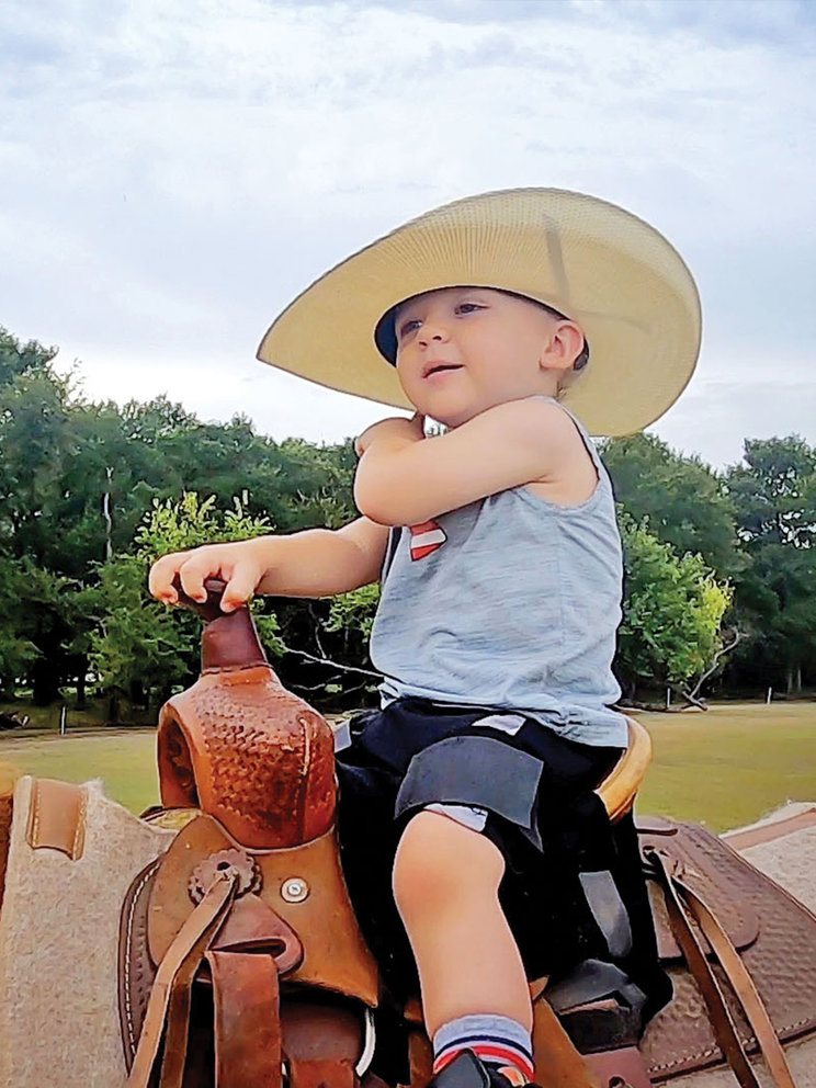 Brady as a toddler, in an oversized cowboy hat, horseback riding